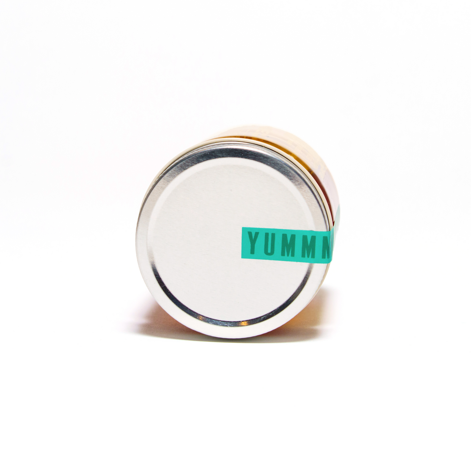 A small jar with a metal lid, seen from above, features a green label with YUMM in bold—ideal for highlighting Honey House Honey Alfalfa Honey and its natural antioxidants. The plain white background keeps focus on the product.