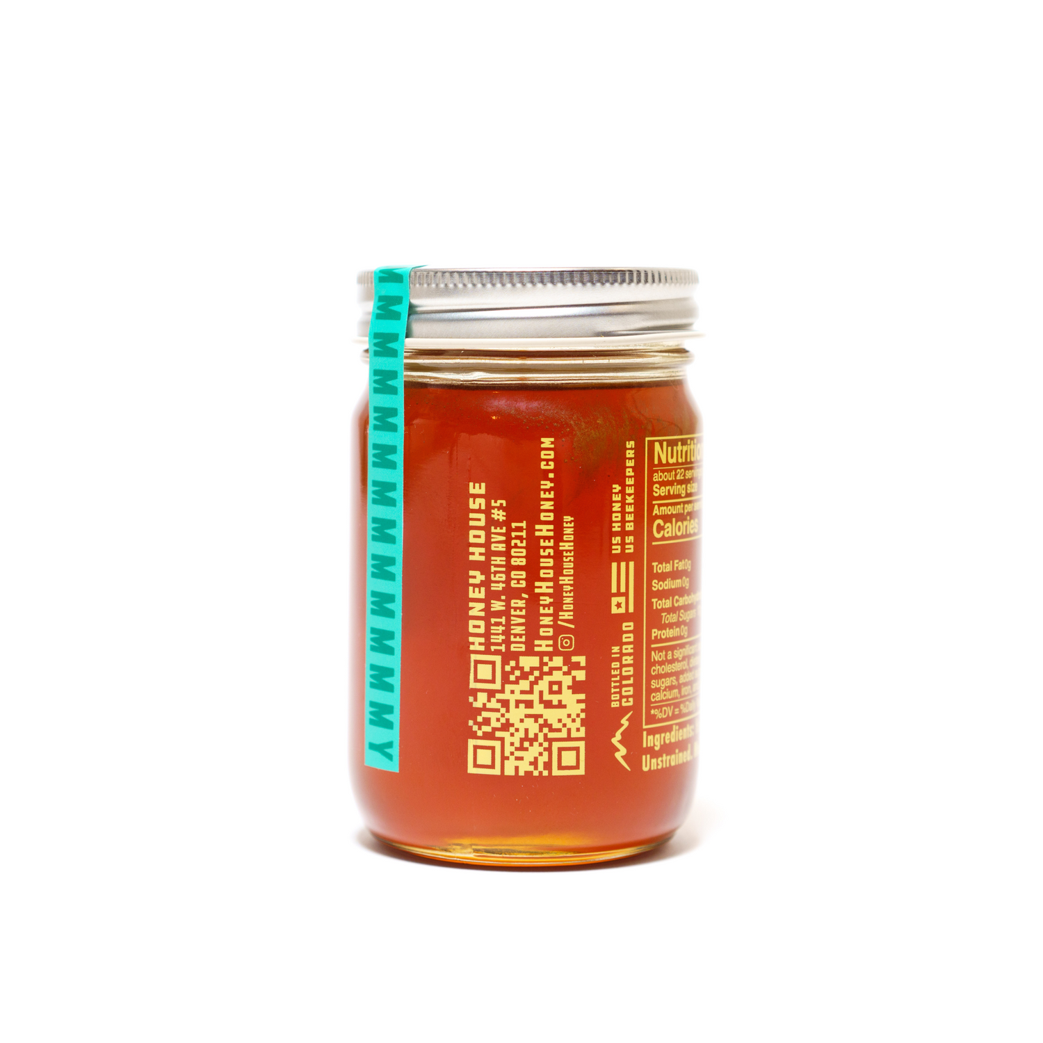 A glass jar of Honey House Honey Alfalfa Honey, sealed with a metal lid and teal tamper-evident strip, features orange and white text, a QR code, and nutrition facts that highlight its natural antioxidants.