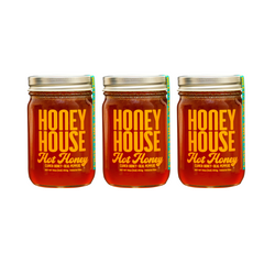 Three jars of Honey House Honey Hot Honey, made with raw honey and real peppers, are displayed side by side on a white background. Each jar features a metal lid and bold yellow and red branding.
