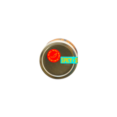 A round metal tin viewed from above with a red sticker featuring a chili pepper and the words SPICY x SPICY, hinting at natural heat, on a blue and yellow label partially visible around the edge. Product: Hot Honey by Honey House Honey.